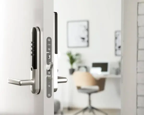 Modernt digitalt låssystem på en vit dörr. I bakgrunden syns ett kontor med skrivbord och stol.