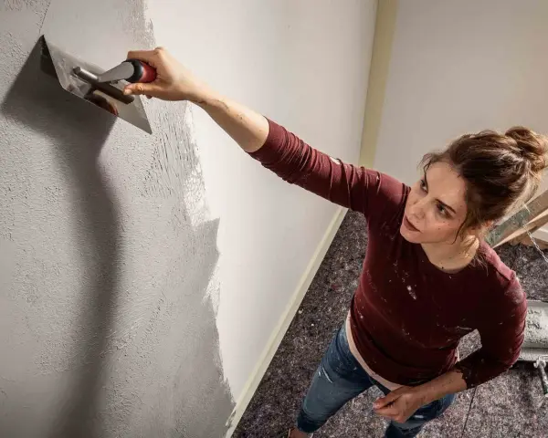 Frau trägt mit einem Spachtel eine Struktur auf die Wand auf. Die Spachteltechnik Wand verleiht dem Raum eine besondere Optik.