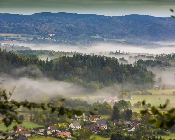 Mgliste poranki nad Sudetami. W oddali widać zamek, a niżej rozciągają się lasy i urokliwe miejscowości.
