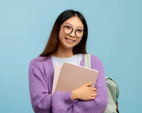 Ragazza con occhiali nuovi per astigmatismo, sorride tenendo libri e zaino.
