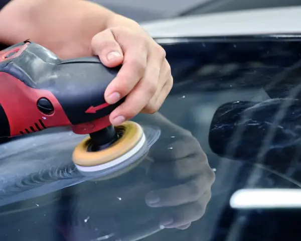 En hand polerar en bilruta med en polermaskin. Glaspolish ger en perfekt finish.