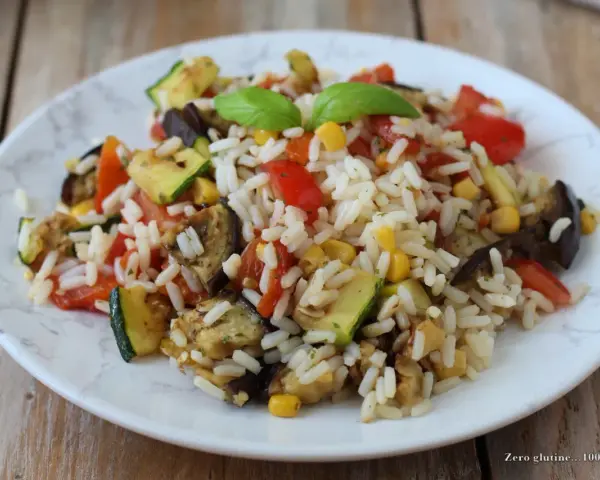 Un piatto colorato di insalata di riso vegetariana con zucchine, melanzane, pomodori e mais, guarnito con basilico fresco.
