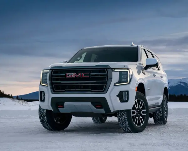 Biały GMC Yukon XL gotowy na zimową przygodę na ośnieżonej drodze, z górami w tle.