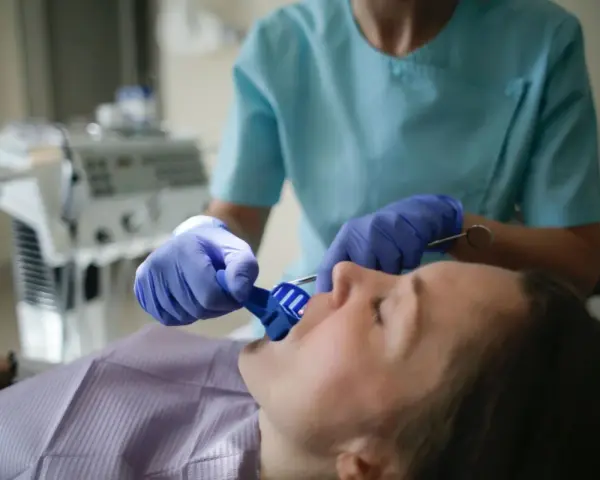 Dentysta w rękawiczkach zakłada pacjentowi niebieski retraktor jamy ustnej.