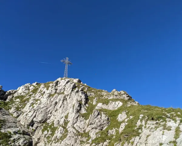 Szlak na Giewont prowadzi przez skaliste zbocza porośnięte trawą. Na szczycie widoczny metalowy krzyż.