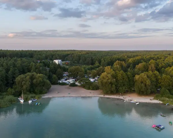 Widok na kemping nad najczystszym jeziorem w Polsce. Woda jest turkusowa, a brzeg piaszczysty. W oddali las.