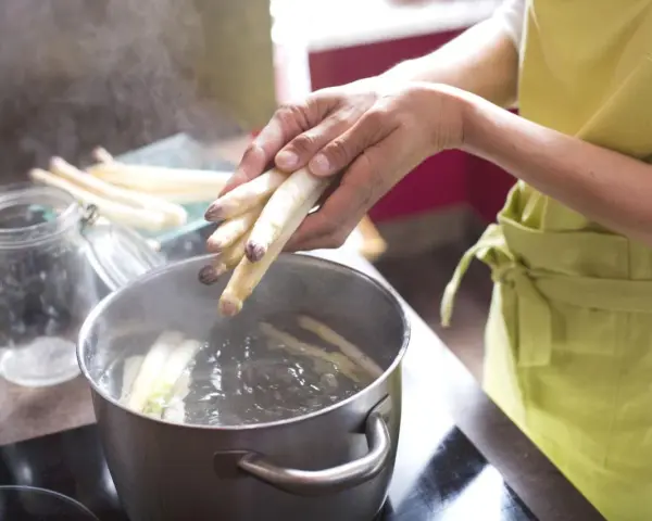 Frischer weißer Spargel wird in kochendes Wasser gegeben. Die Frage, wie lange muss Spargel kochen, beschäftigt viele Hobbyköche.