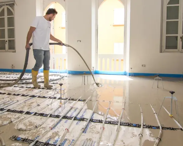 Operaio versa materiale autolivellante su pavimento esistente con riscaldamento a pavimento.