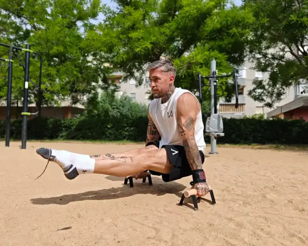 Un homme musclé exécute un exercice de calisthenics, jambes tendues, dans un parc. Un entraînement complet pour un corps athlétique.