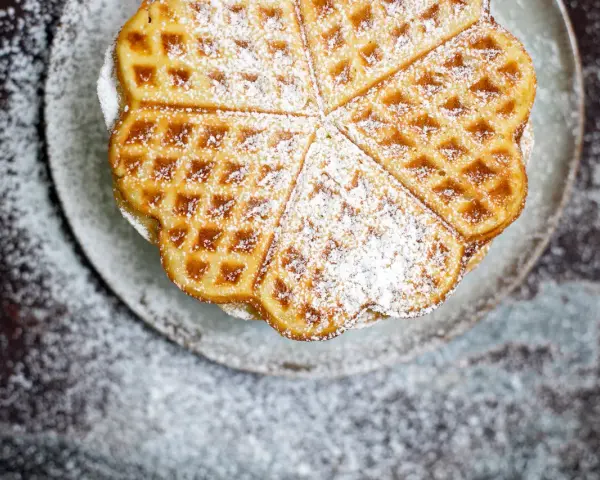 Herzförmige Waffeln, bestäubt mit Puderzucker, auf einem Teller. Ein köstliches Rezept für süße Momente.