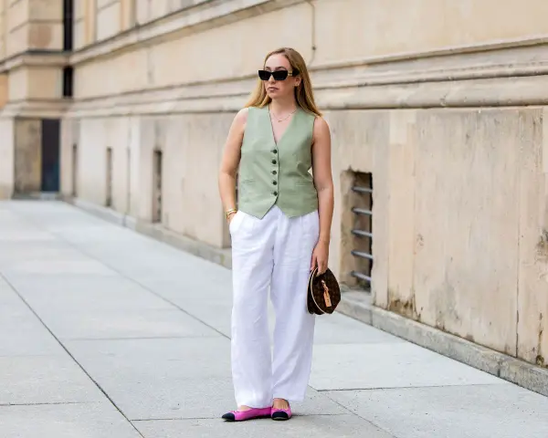 Mujer con un outfit de chaleco verde y outfit pantalon lino blanco, gafas de sol y bolso de mano.