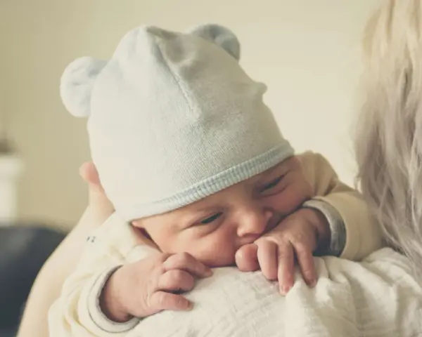 Nyfödd bebis med mössa med öron, tryggt vilande mot en axel. En perfekt baby gåva.