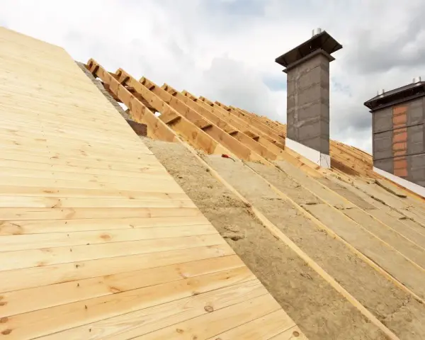 Costruzione tetto con isolamento termico: legno, lana di roccia e camini in muratura sotto un cielo nuvoloso.