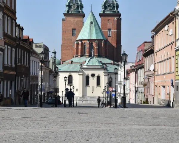 Spacer po brukowanym rynku Gniezna, z katedrą w tle. Kolorowe kamienice po bokach tworzą urokliwą atmosferę.
