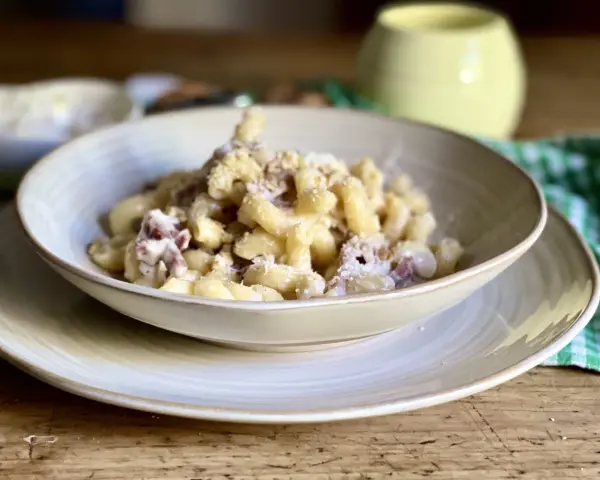 Piatto di pasta con prosciutto crudo, formaggio grattugiato e una salsa cremosa. Un classico confortante.