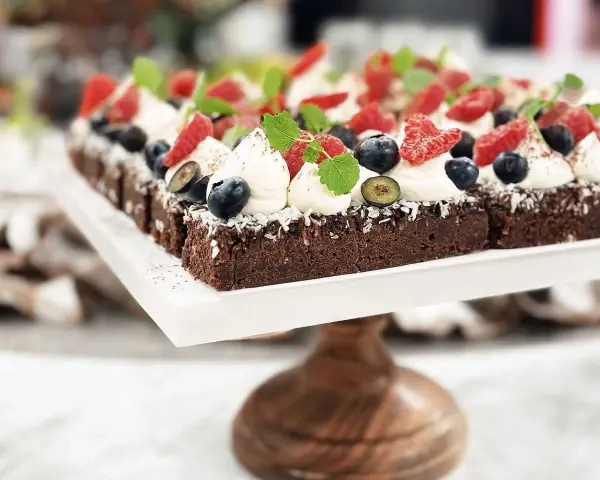 En rad läckra bitar kladdkaka med fudge, toppade med vispad grädde, färska bär och mynta.