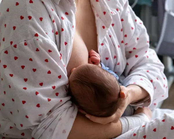 Matka karmi piersią dziecko. W tle widać łóżeczko. Zatkany kanał mleczny to częsty problem.