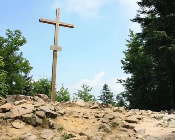 Drewniany krzyż na skalistym szczycie, najwyższy szczyt w górach świętokrzyskich, otoczony zielenią drzew.