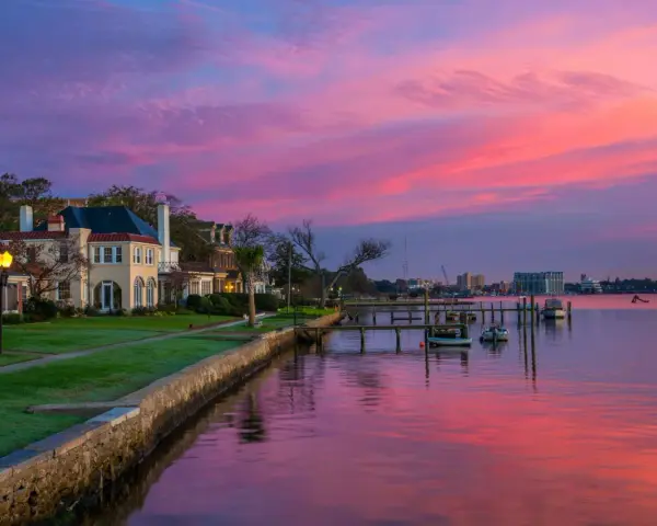 Beautiful waterfront homes and boats reflect a vibrant pink and purple sunset, perfect for weekend trips from Richmond, VA.