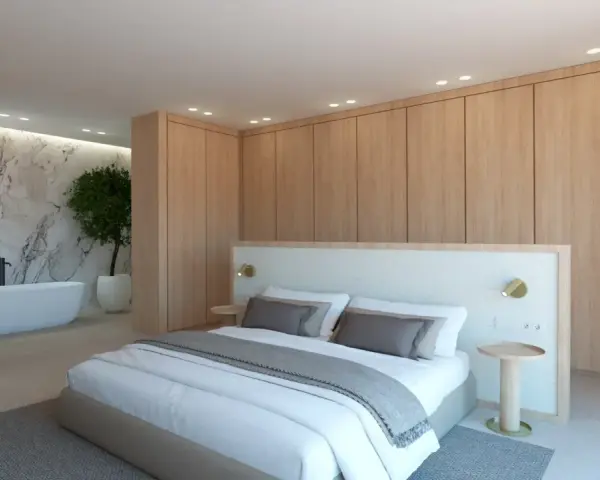Elegante dormitorio con armarios de madera clara y detalles blancos. La cama, con ropa de cama blanca y cojines grises, se combina perfectamente con la pared de mármol y la bañera.