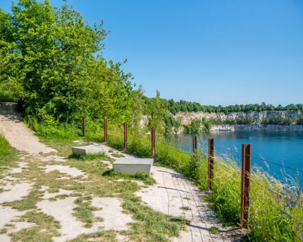 Ścieżka spacerowa nad turkusową wodą w kamieniołomie. Zakrzówek trasa zachęca do odpoczynku na ławkach wśród zieleni.