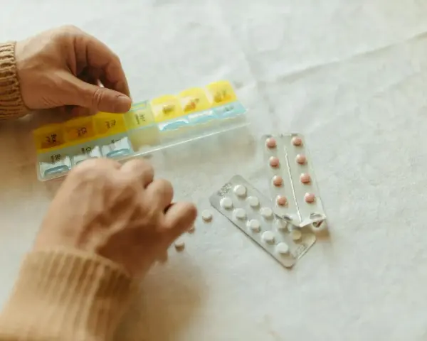 Dłonie układają tabletki w organizerze. Obok leżą blistry. Gdzie kupić tabletki antykoncepcyjne bez recepty?
