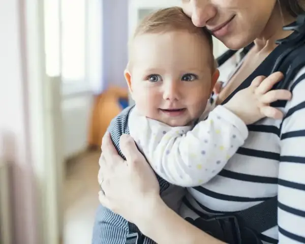 Uśmiechnięte dziecko w nosidle od urodzenia, przytulone do mamy.