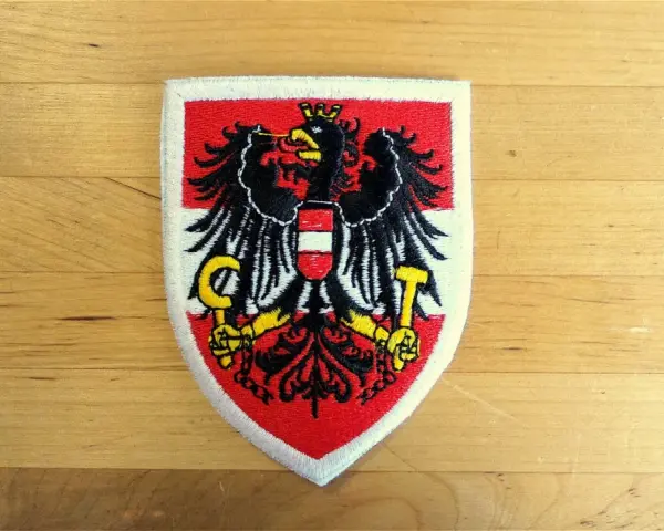 Naszywka z godłem Austrii: czarny orzeł z tarczą w biało-czerwone pasy, trzymający sierp i młot.