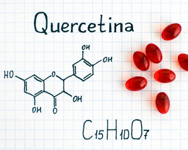 Fórmula química de la quercetina, un flavonoide con propiedades antioxidantes, junto a cápsulas rojas.