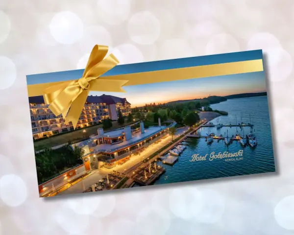 Złota karta Gołębiewski jak otrzymać? Voucher na pobyt w Hotelu Gołębiewski Mikołajki, ozdobiony złotą wstążką.