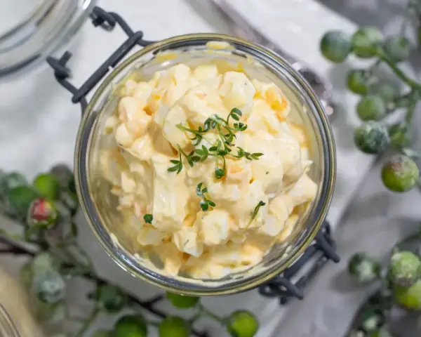 Cremiger Kartoffelsalat mit Fleischsalat, garniert mit frischen Kräutern, in einem Glas serviert.