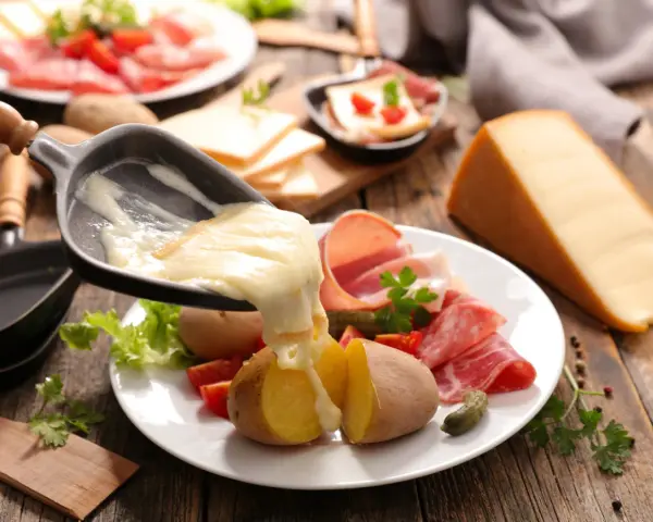 Roztopiony ser z patelni do raclette spływa na ziemniaki i wędliny. Pyszne danie raclette.