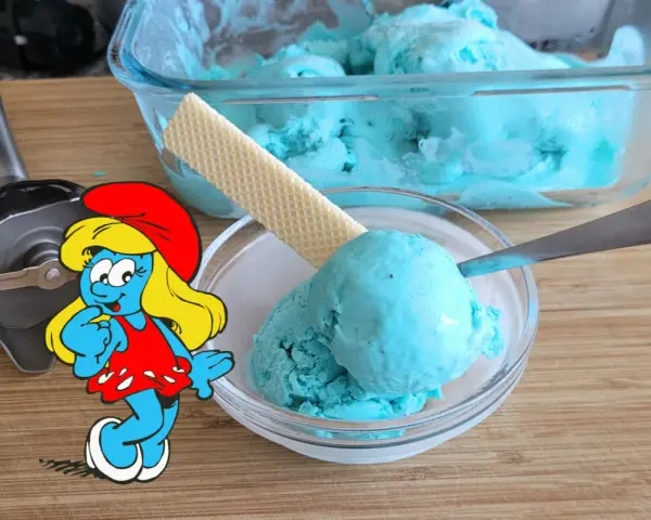 Schlumpfine genießt engelblaues Eis. Ein Handmixer und ein Waffelblatt liegen daneben.