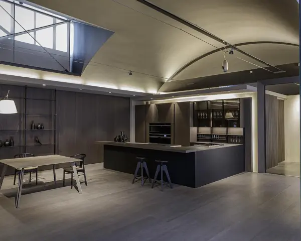 Moderna cocina office con isla central, muebles oscuros, estanterías y mesa de comedor.