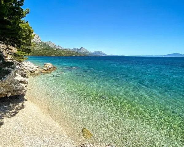 Idealne miejsce na camping w Chorwacji: kamienista plaża, turkusowa woda i góry w tle.