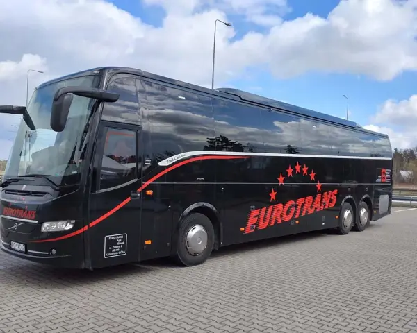 Czarny autokar turystyczny Eurotrans z czerwonymi gwiazdami i napisem na tle błękitnego nieba.