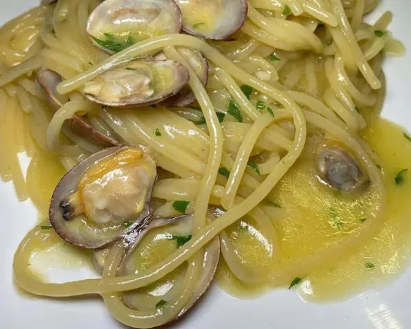 Spaghetti alle vongole cremosi come al ristorante, con vongole fresche e prezzemolo tritato su un letto di pasta dorata.