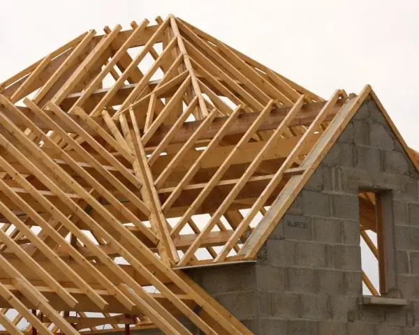 Structure en bois d'une charpente simple, en cours de construction. Les poutres de bois forment un motif complexe au-dessus des murs en blocs de béton.