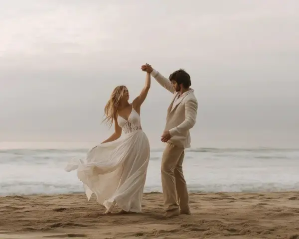 Coppia felice balla sulla spiaggia. Lui indossa un completo chiaro, perfetto per un matrimonio in spiaggia come vestirsi uomo.
