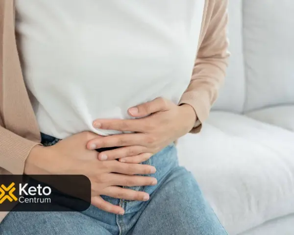 Kobieta trzyma się za brzuch, szukając odpowiedzi na pytanie, co jest dobre na jelita. Logo Keto Centrum.