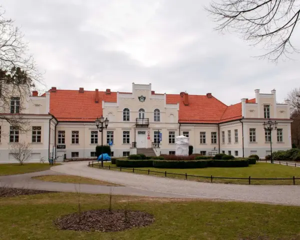 Pałac Przebendowskich w Wejherowie, z czerwonym dachem i kremową fasadą, otoczony zielenią i drzewami.
