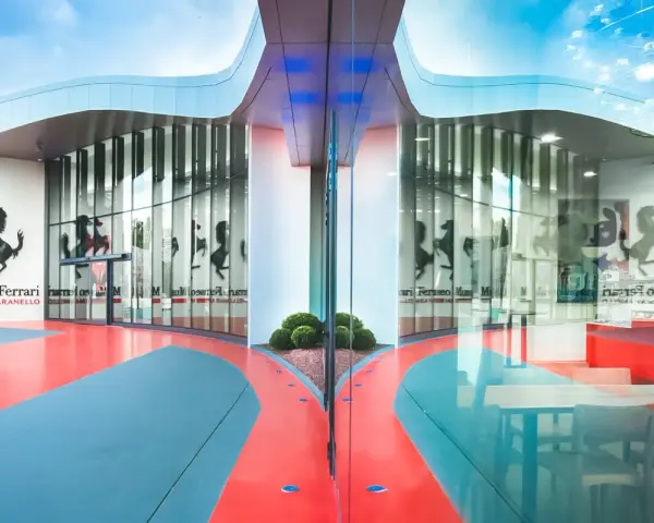 Nowoczesne muzeum Ferrari w Maranello, z charakterystycznym logo i odbijającymi się w szkle sylwetkami koni.
