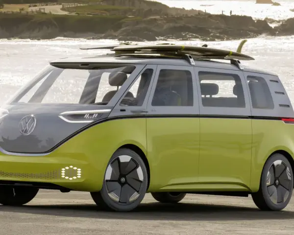 Volkswagen ID. Buzz w kolorze limonkowym z deskami surfingowymi na dachu, nad morzem.