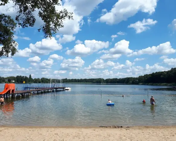 Sommerfreude im Strandbad Heiligensee: Kinder planschen, ein Mann kühlt sich ab, eine Rutsche lockt. Blauer Himmel mit weißen Wolken.