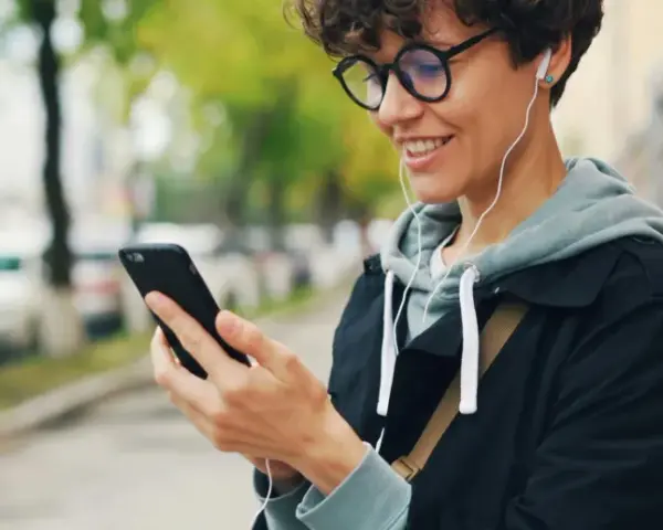 Uśmiechnięta osoba w słuchawkach patrzy na telefon. Czy wiesz, co to jest impedancja w słuchawkach i jak wpływa na dźwięk?