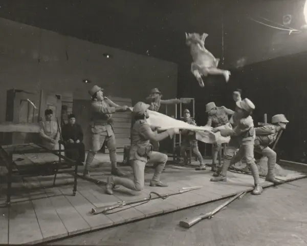 Scena teatralna: żołnierze w mundurach z epoki, jeden w powietrzu, trzymają białą tkaninę. Kantor Wielopole.