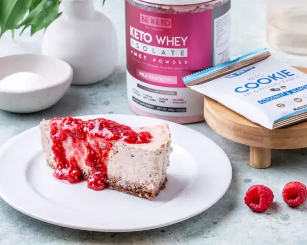 Pyszny sernik keto z malinami, obok słoik Keto Whey Isolate i batonik Keto Cookie. Idealny keto spod do sernika.