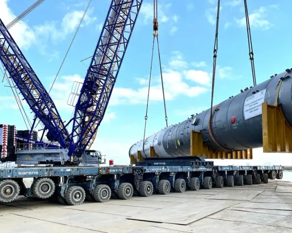 Największy transport w Polsce: potężny dźwig Sarens podnosi ogromny element instalacji na wielokołową platformę.