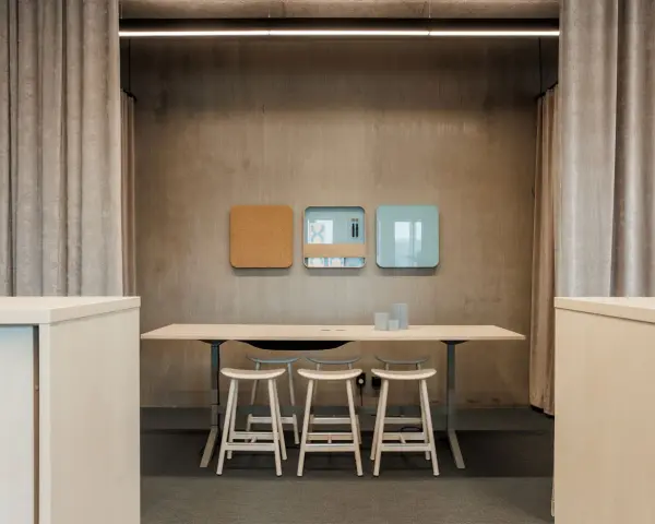 En modern och inredd verkstad med ett långt bord, pallar och anslagstavlor på väggen.