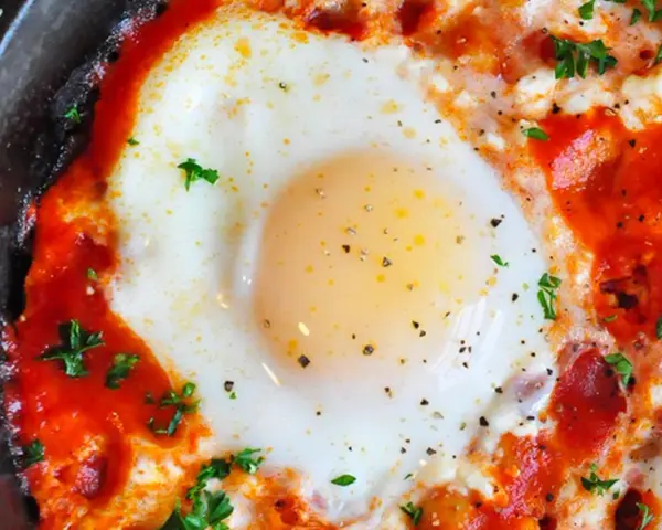 Uova al pomodoro, un piatto saporito con uovo cotto in salsa di pomodoro e formaggio, guarnito con prezzemolo fresco.